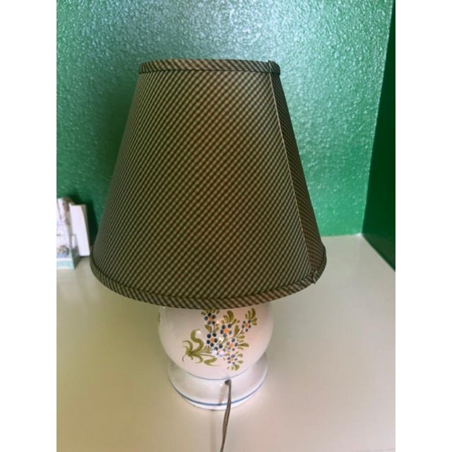 This charming table lamp features a rounded white ceramic base adorned with a hand-painted floral wreath design with...