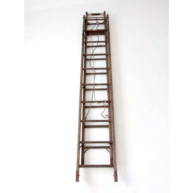 Early 20th century Oshkosh Patented Safety Ladder featuring weathered wood rails, iron hardware, and original pulley...