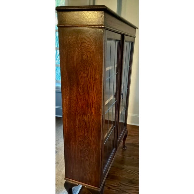 An elegant English Revival oak bookcase or display cabinet dating to approximately 1900–1920. Featuring an unusually...