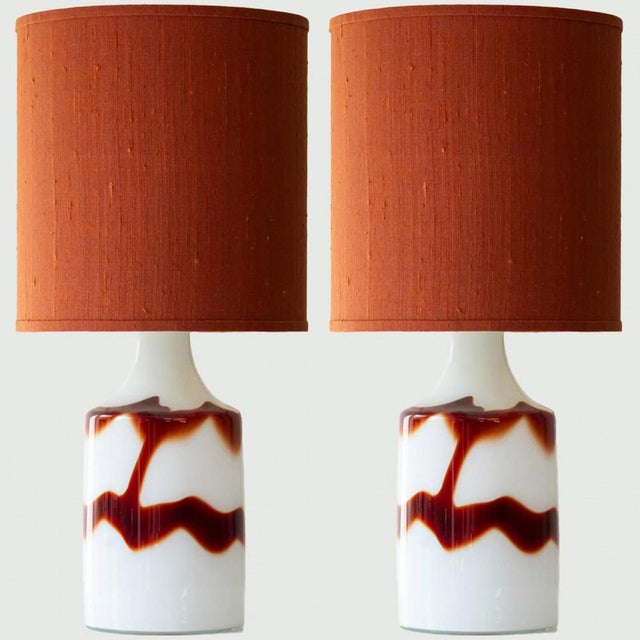 Pair of heavy quality opal glass table lamps by Holmegaard, 1970s. The design is called ‘Flame’ and features a ox blood...