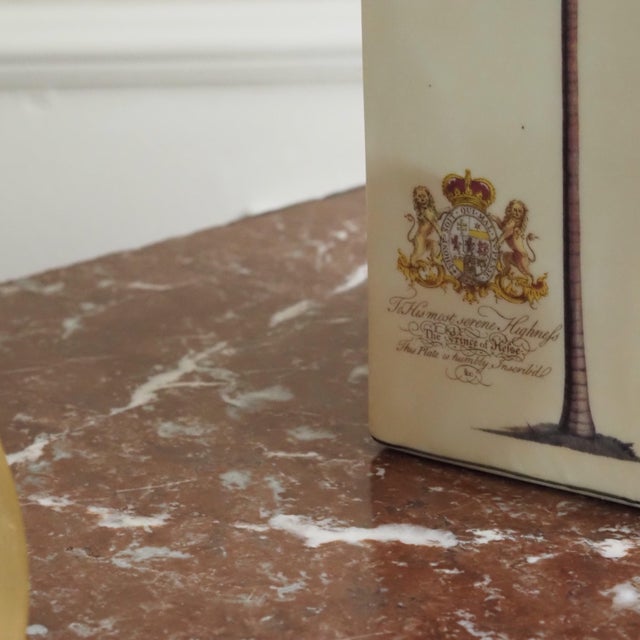 Square ceramic box in cream with detailed palm illustrations and a royal coat of arms on all four sides. The decoration is...