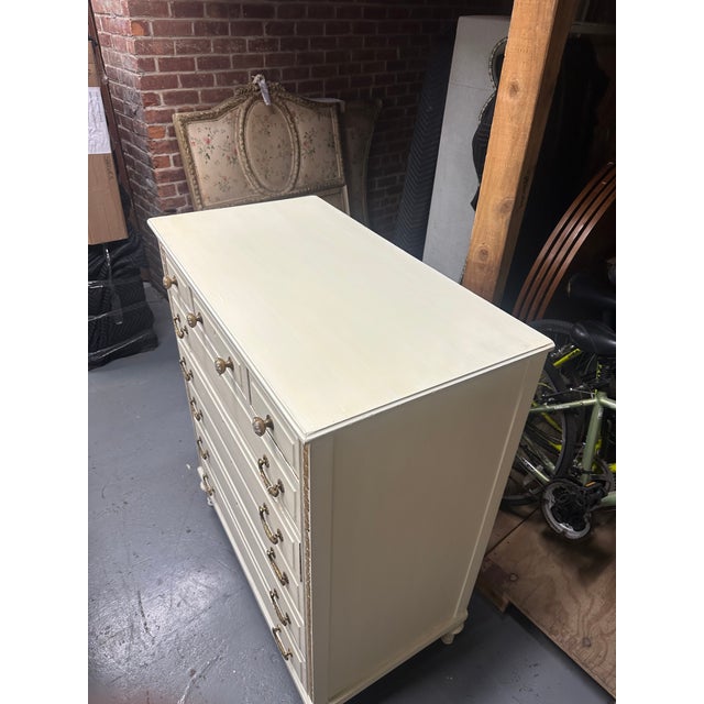 Early 20th Century French Country Chest of Drawers, crafted in solid wood and finished in off-white and gold paint. The...