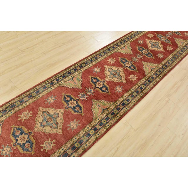 A tribal Kazak runner hand-knotted with fine wool on a cotton foundation. This oriental rug features a row of medallions...