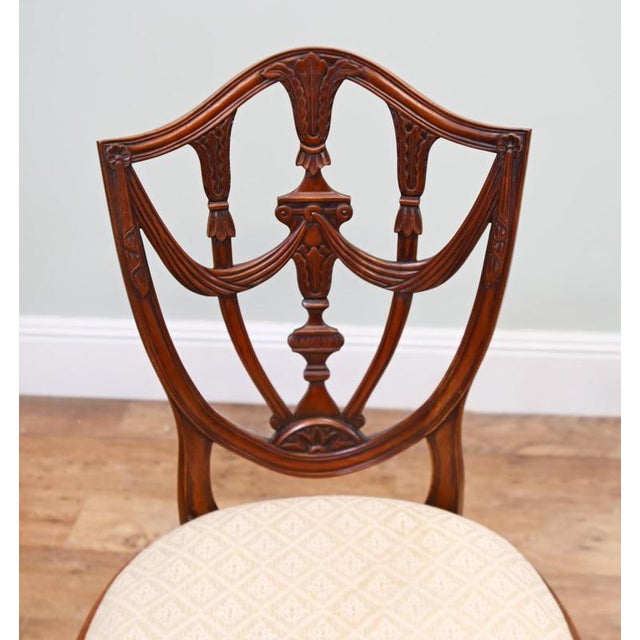 An elegant pair of dining chairs in the Hepplewhite style Each shield-shaped back is decorated with carved swags, a turned...