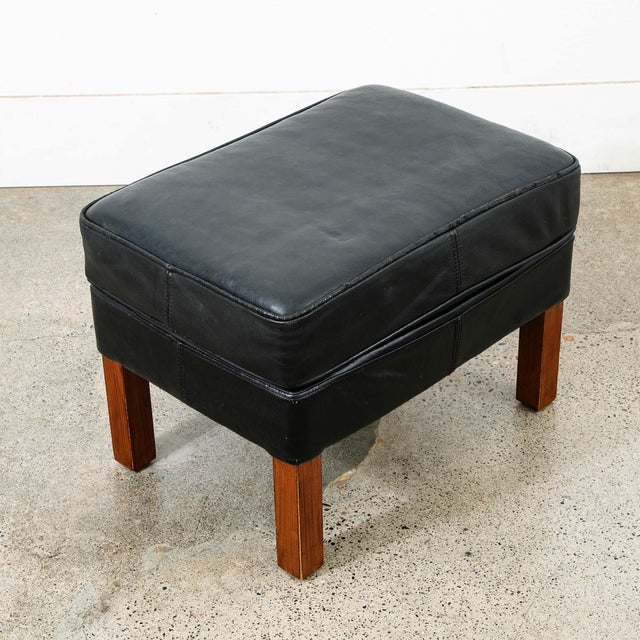 Danish modern black leather ottoman / footstool with wood legs. Unknown maker. Recently imported from Denmark.