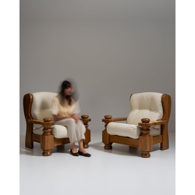 This pair of 1970s Brutalist oak upholstered armchairs from France, made in chunky carved oak with cream cushions. The...