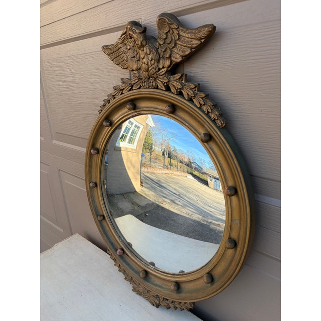 A gorgeous Federal or Regency style convex bullseye wall mirror featuring a carved eagle with open wings standing on olive...