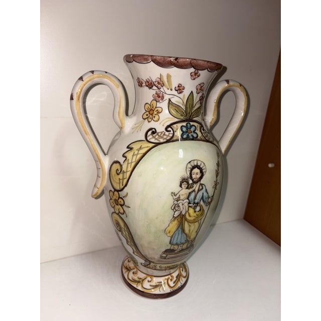 Hand-painted majolica ceramic vase with handles depicting Saint Joseph with the Baby Jesus and featuring delicate floral...