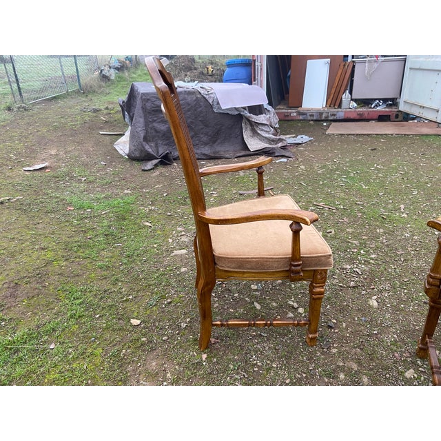 The product is a set of two vintage walnut/cane back dining armchairs, featuring a medium brown wood and pale yellow...