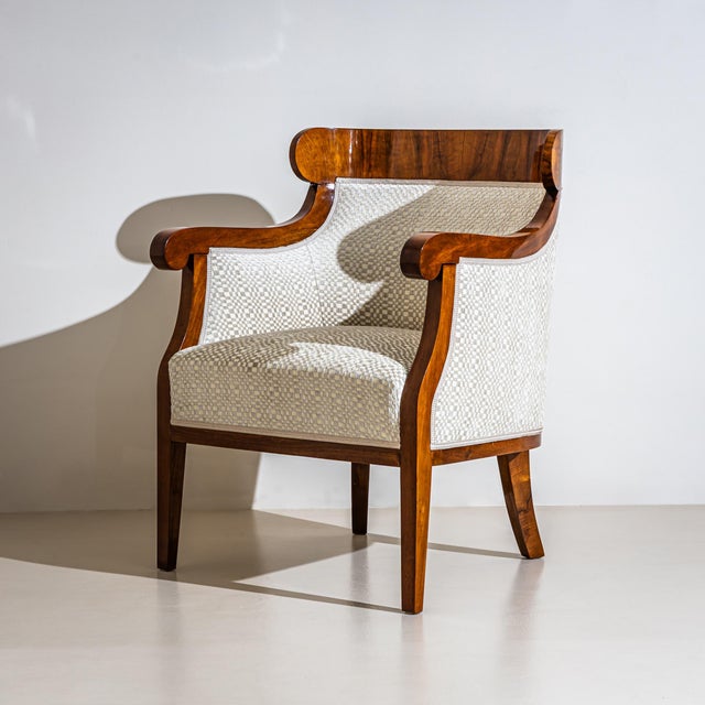 Pair of Biedermeier-style bergères with walnut-veneered frames and armrests ending in stylized volutes. The armchairs have...