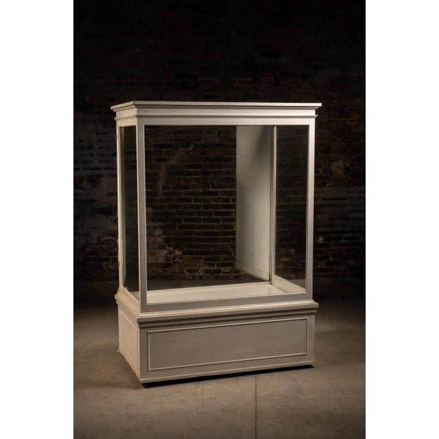 Large freestanding retail display showcase constructed with a painted wood frame, glass front and side panels, glass top,...