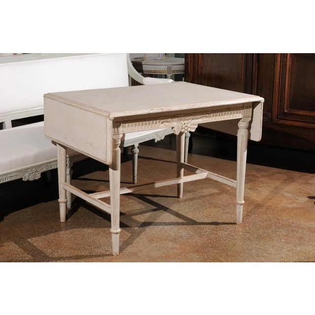 A Swedish neoclassical style painted wood drop-leaf table from the early 20th century, with carved apron, fluted legs and...