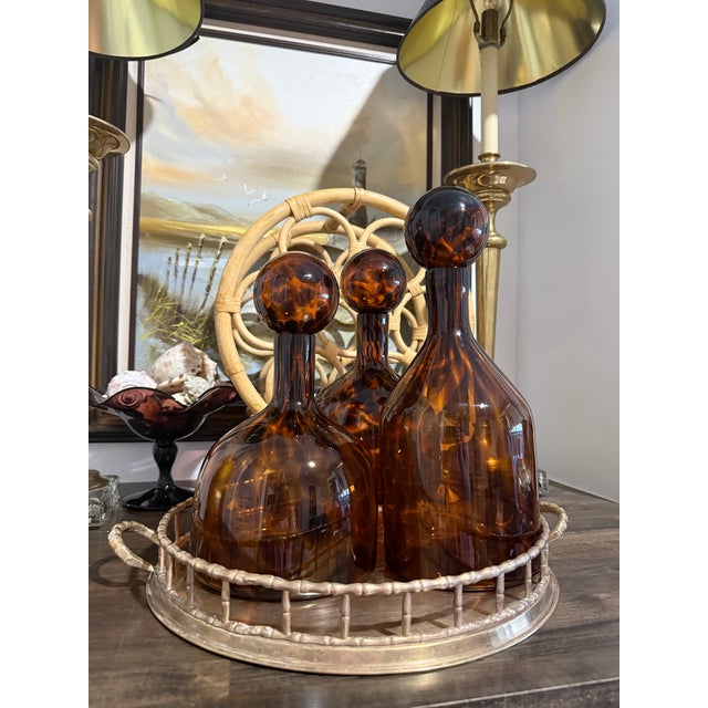 A striking set of three tortoise glass decanters in rich amber and brown tones, each finished with an oversized round...