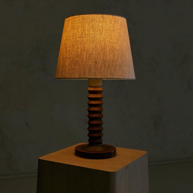 A French table lamp from the 1950s, attributed to Charles Dudouyt. The turned wooden base rises in a rhythm of stacked...