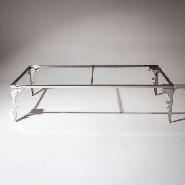 Rectangular coffee table in stainless steel with sculptural cut-out legs and a smoked glass top. The guarantee label is...