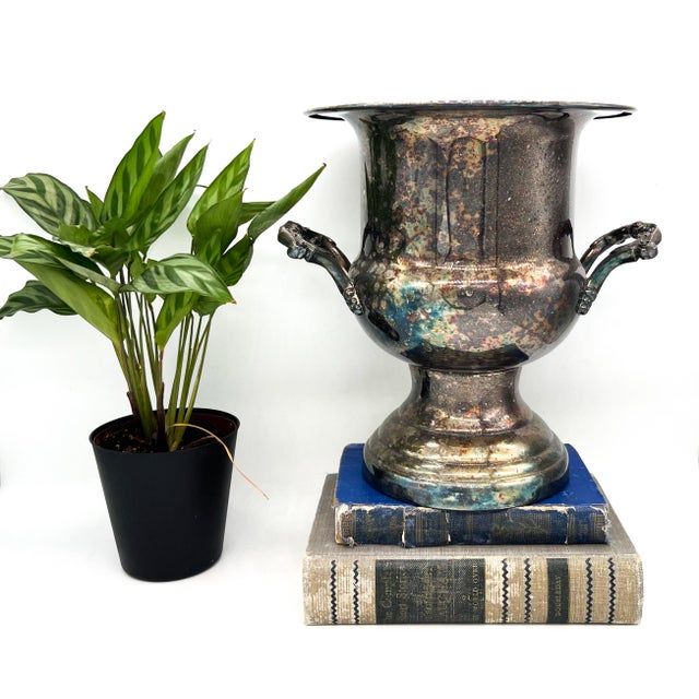 A silver plate trophy urn / champagne bucket with a flared rim, pedestal base, and ornate floral handles. The front is...