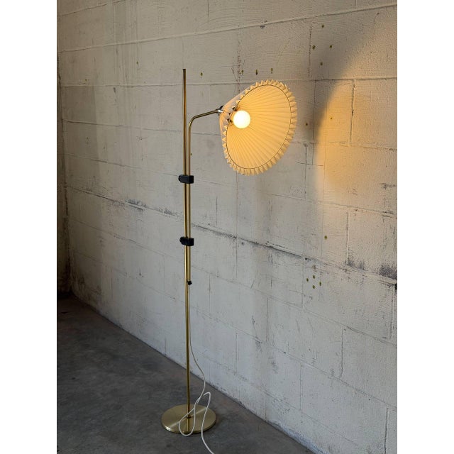 This adjustable brass floor lamp features a slender stem and a classic pleated shade casting warm ambient light. Designed...
