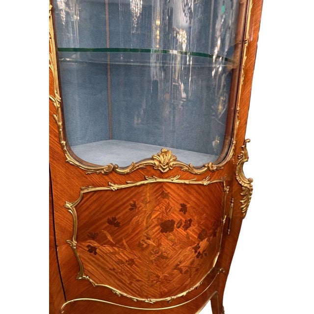 An elegant 19th-century French Louis XV-style vitrine, finely crafted with richly figured wood veneers, floral marquetry,...