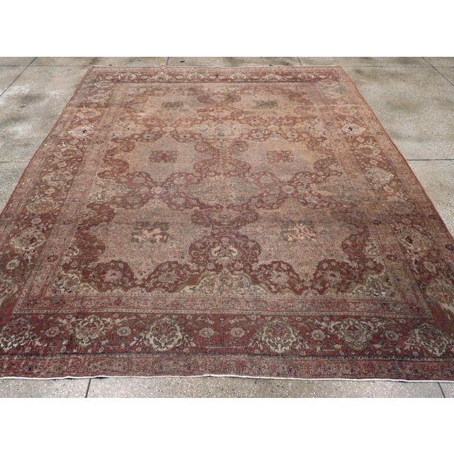 This early 20th-century Persian Isfahan room-size carpet presents a richly layered floral composition in muted rose, soft...