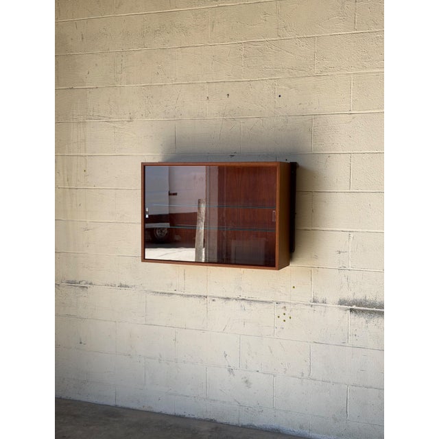 Beautiful vintage Danish teak wall-mounted display cabinet by Cado, featuring clean architectural lines, warm wood tones,...