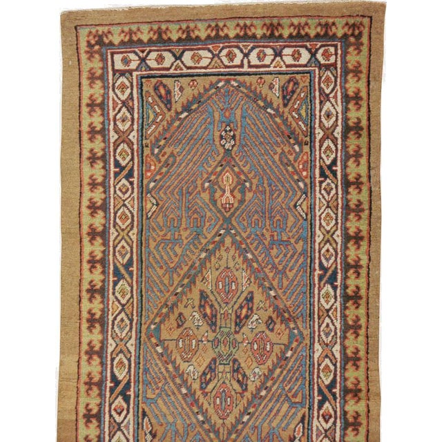 This early 20th-century Persian Serab runner presents a finely organized tribal composition across a warm camel and soft...