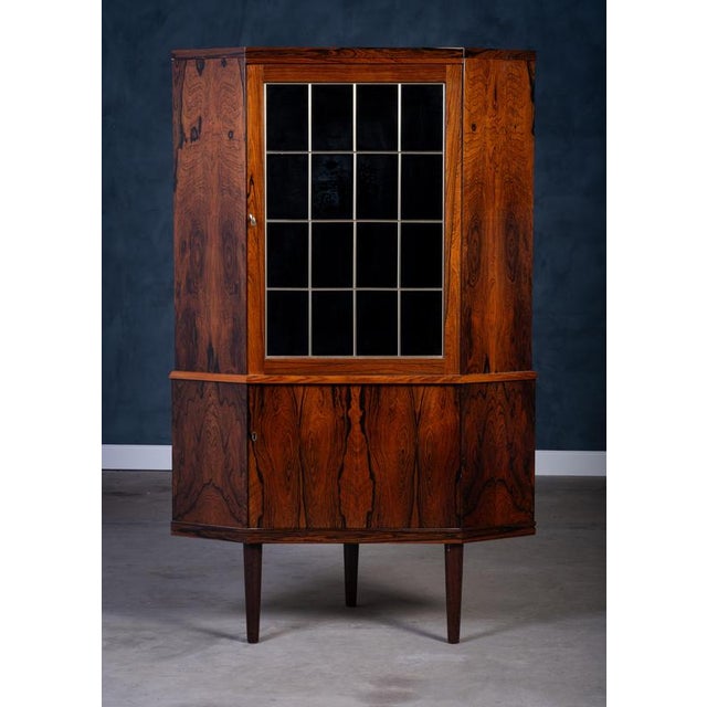 Elegant Danish corner cabinet from the 1960s crafted in richly grained rosewood. Features beautiful leaded dark glass and...