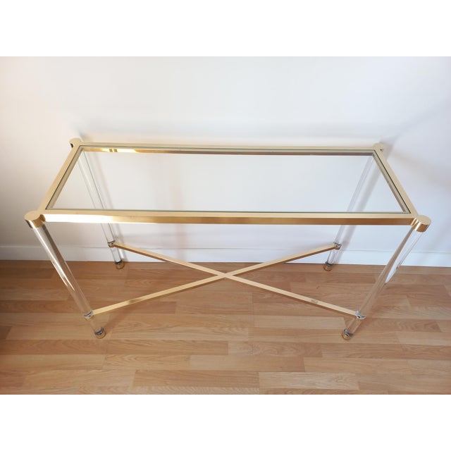 Rectangular design console in lucite and gold metal, glass top. The tubular base is connected by an X-shaped spacer. Good...