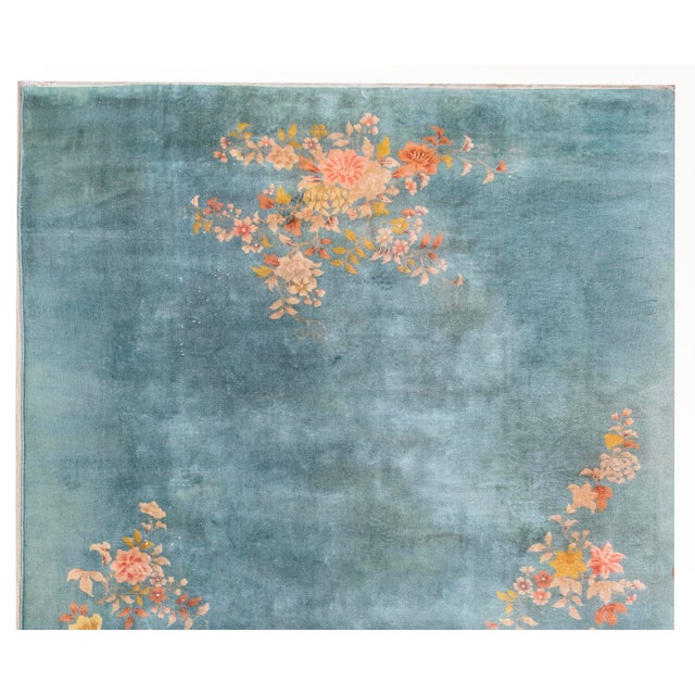 This vintage Chinese Art Deco rug features a serene teal-blue field adorned with elegant floral sprays. Hand-woven in the...