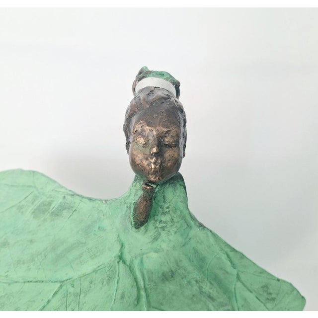 This striking artwork features a delicate figure poised on a textured stone base. The sculpture captures a dancer,...