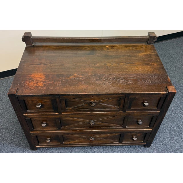 A striking three-drawer chest with a rich dark wood finish and rustic, architectural character. Each drawer features a...