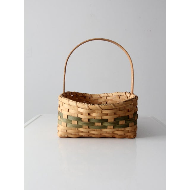 This vintage handmade gathering basket features warm honey-toned wicker with a subtle muted green accent woven through the...