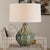 Graced With A Subtly Swirled Ceramic Base, This Elegant Table Lamp Showcases A Harmonious Blend Of Muted Greens And Blue...