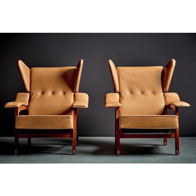 Pair of lounge chairs with angular walnut frames and winged backs. The chairs are defined by their deeply pitched seats,...