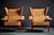 Pair of lounge chairs with angular walnut frames and winged backs. The chairs are defined by their deeply pitched seats,...