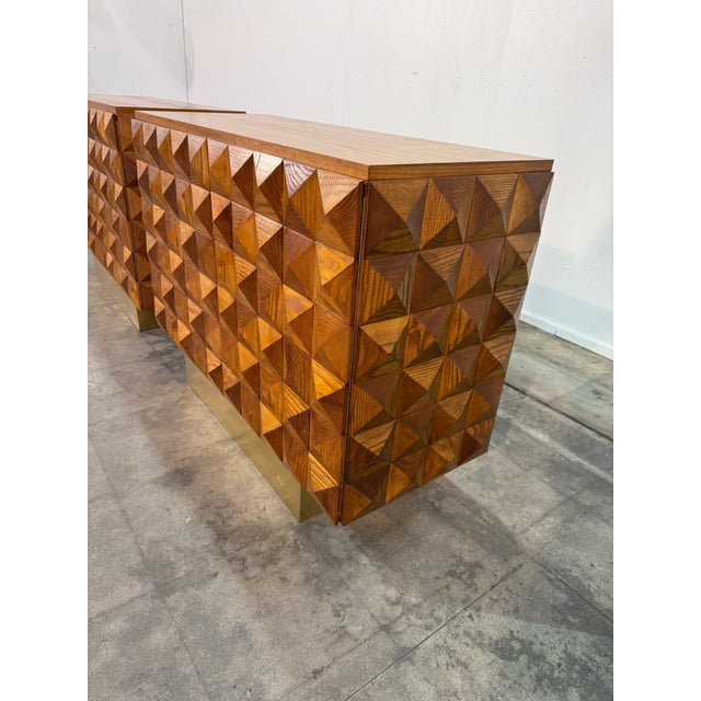 This striking pair of cabinets showcases a bold geometric façade composed of hand-carved, faceted wooden panels that...
