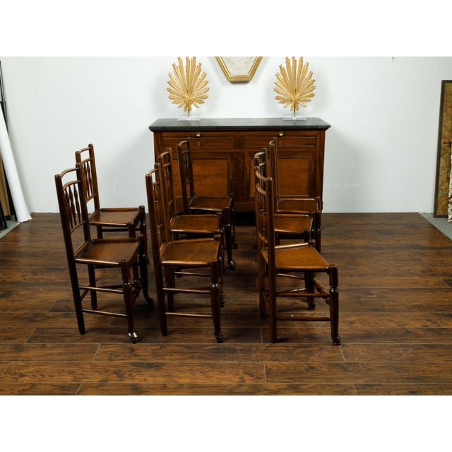 An English set of eight oak dining room side chairs from the late 19th century, with spindle motifs and wooden seats....