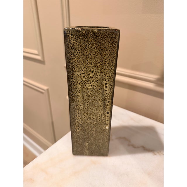 A sculptural rectangular ceramic vase featuring a richly textured speckled glaze in earthy tones of olive, charcoal, and...