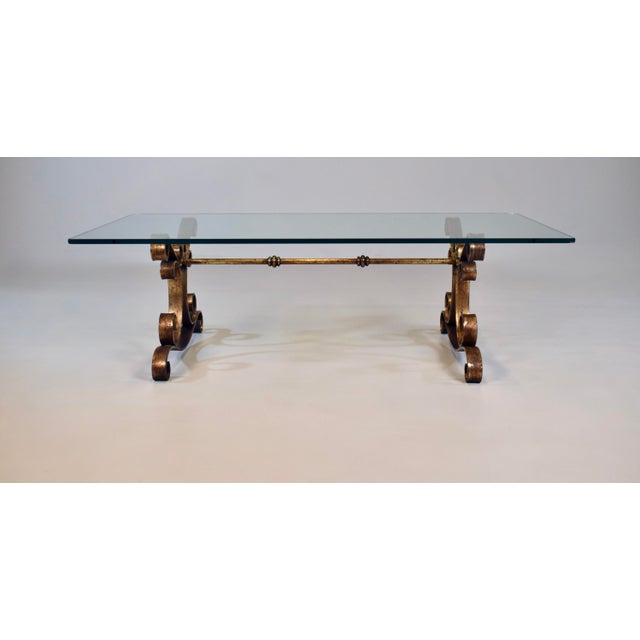 A 1960s gold gilt iron and glass Spanish/Hollywood Regency coffee table featuring scrolling, hand-gilded wrought iron base...
