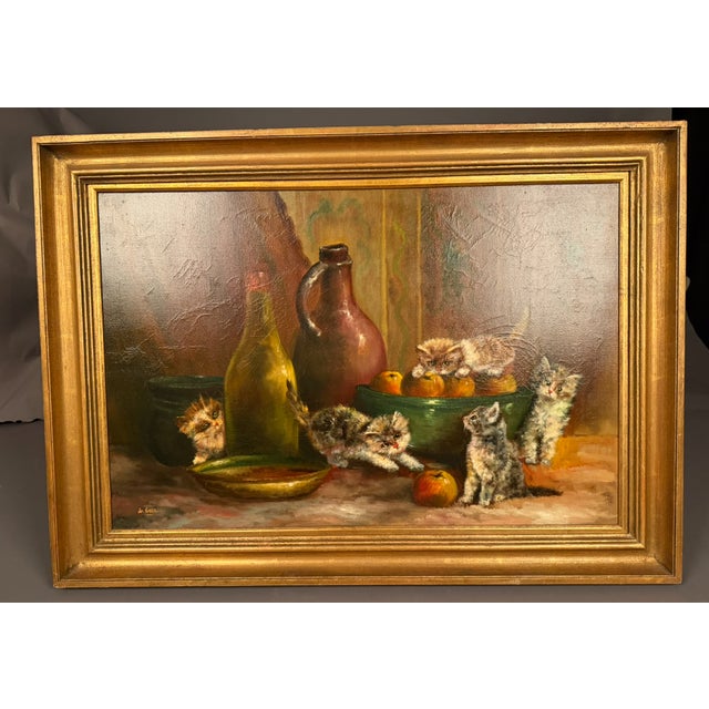 French oil on canvas depicting a still life with kittens, fruit, bottles, and bowls. Signed De Beer. Circa 1940. The...