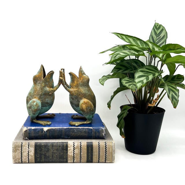 Whimsical vintage pair of bronze frog figurines captured mid “patty cake,” their outstretched hands meeting in a playful,...