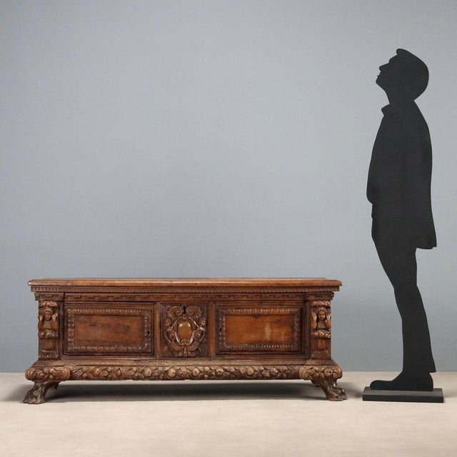 Baroque walnut chest. Paneled front with a central shield depicting a pair of cherubs, ribbons, and curls. Side panels...