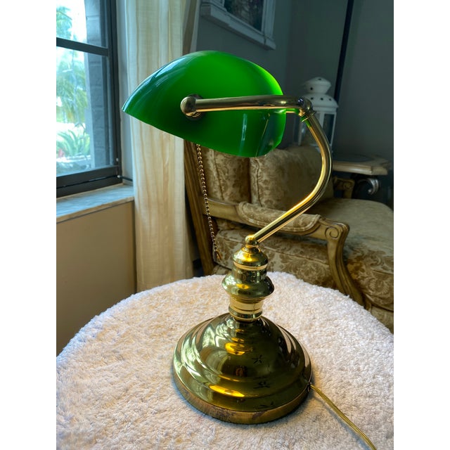 Classic vintage banker’s-style table lamp featuring a distinctive glossy green glass shade, polished brass-tone adjustable...