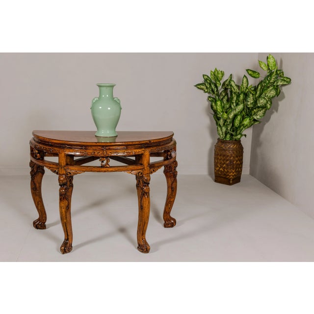 A Qing Dynasty period wooden demilune table from the 19th century with carved apron and mythical creatures on the legs....