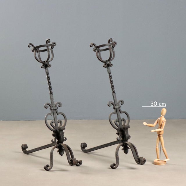 A pair of wrought iron andirons. Tripod front, central lyre decoration, and a cage at the top. This piece is attributed to...