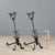 A pair of wrought iron andirons. Tripod front, central lyre decoration, and a cage at the top. This piece is attributed to...