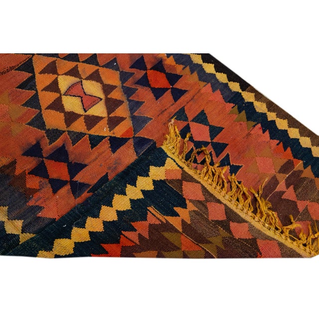 Beautiful kilim handmade wool runner with a rust field. This Vintage flatweave rug has brown, orange, and goldenrod...