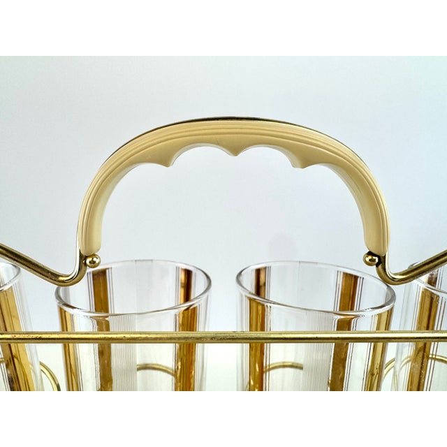 A stylish mid-century cocktail set featuring eight coordinating glasses displayed in their original gold-tone metal...