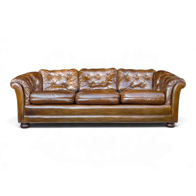 This cognac brown leather sofa offers a relaxed interpretation of classic Chesterfield design. Rolled arms and button...