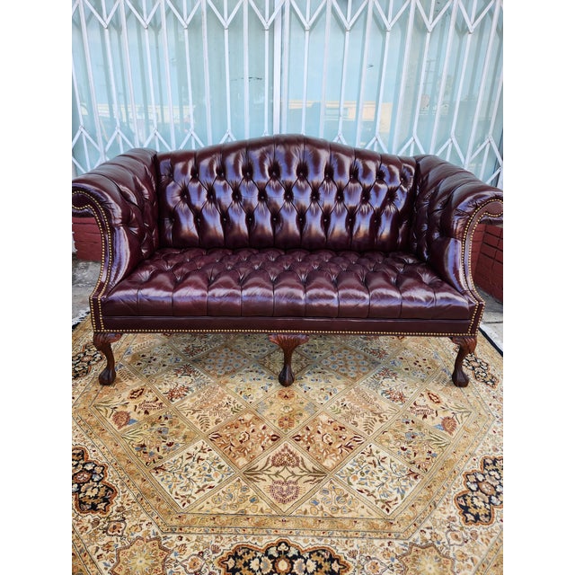 Classic Chesterfield loveseat is upholstered in deep burgundy leather with all-over button tufting on the back, seat, and...