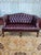 Classic Chesterfield loveseat is upholstered in deep burgundy leather with all-over button tufting on the back, seat, and...